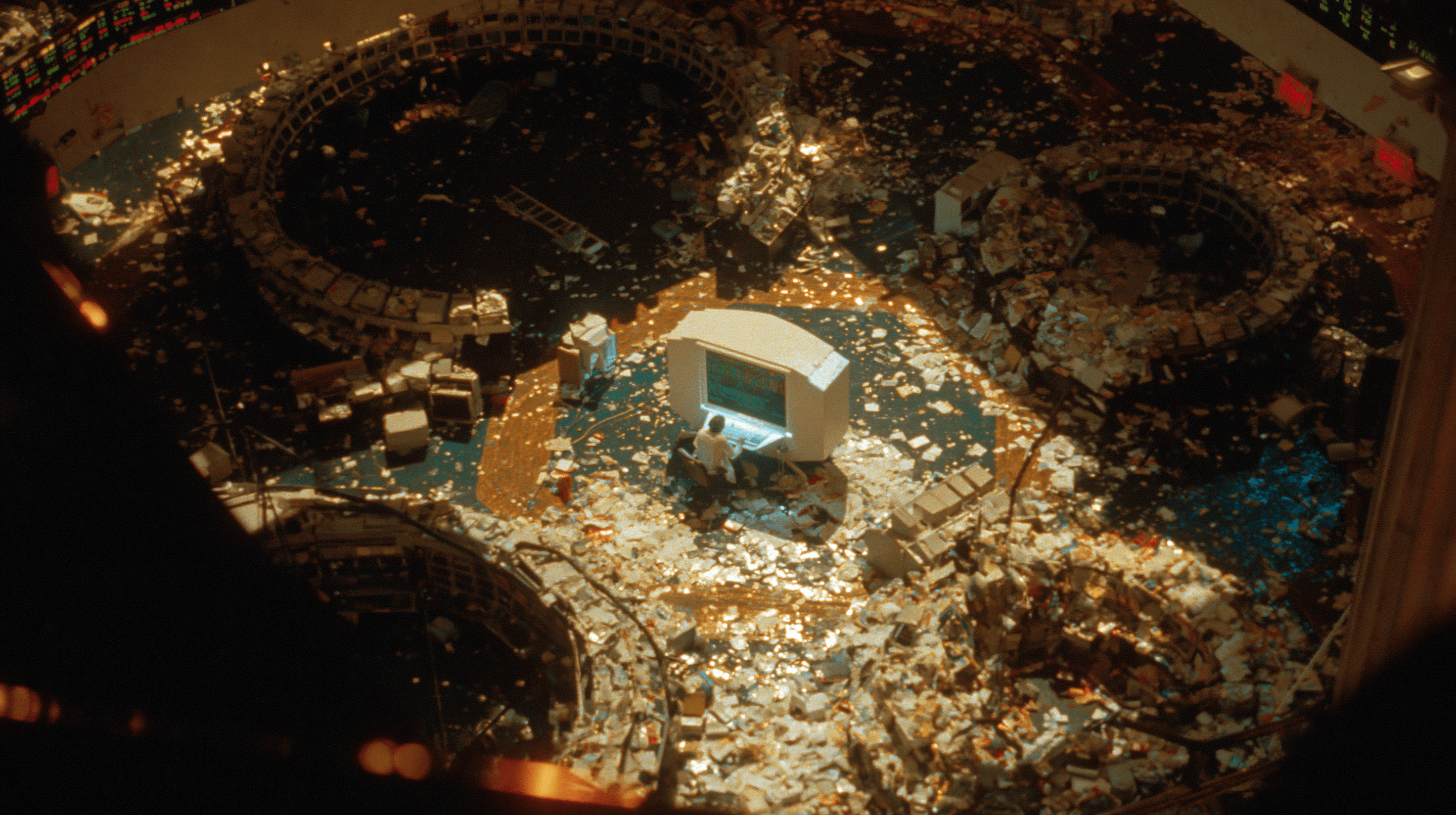 Overhead bird's-eye view of a deserted 1980s Wall Street trading floor, a single operator at the center.